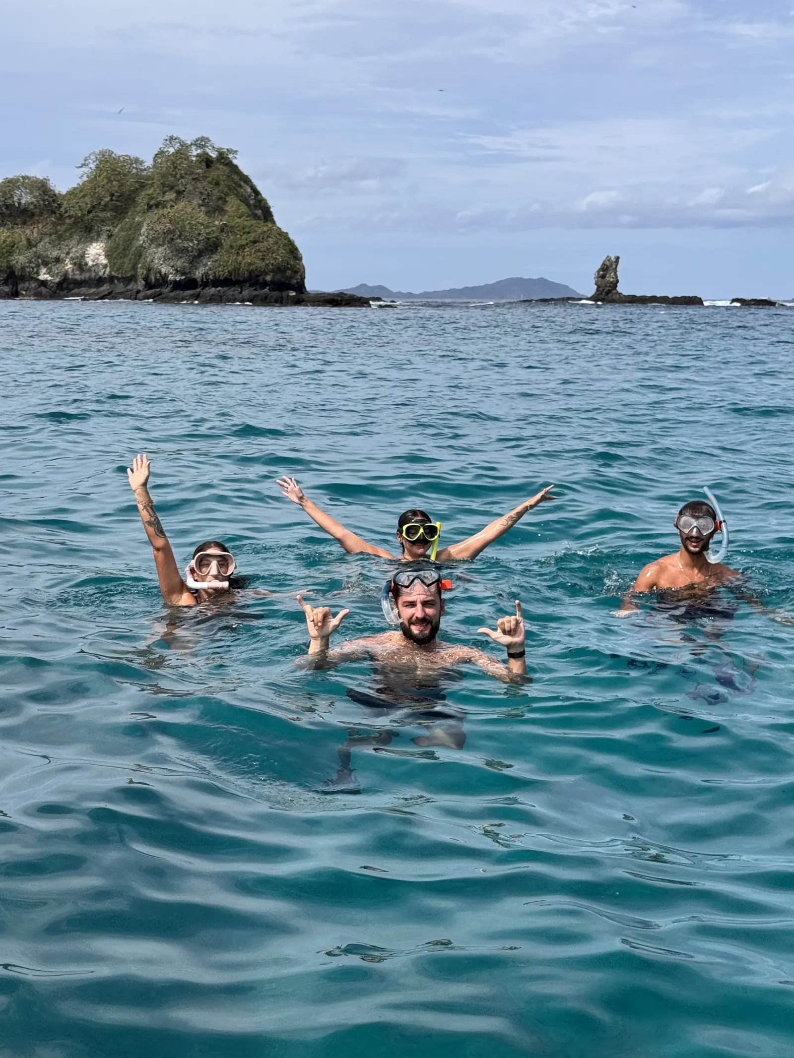 Four guests snorkeling in the water off Playa Flamingo, masks on and hands up